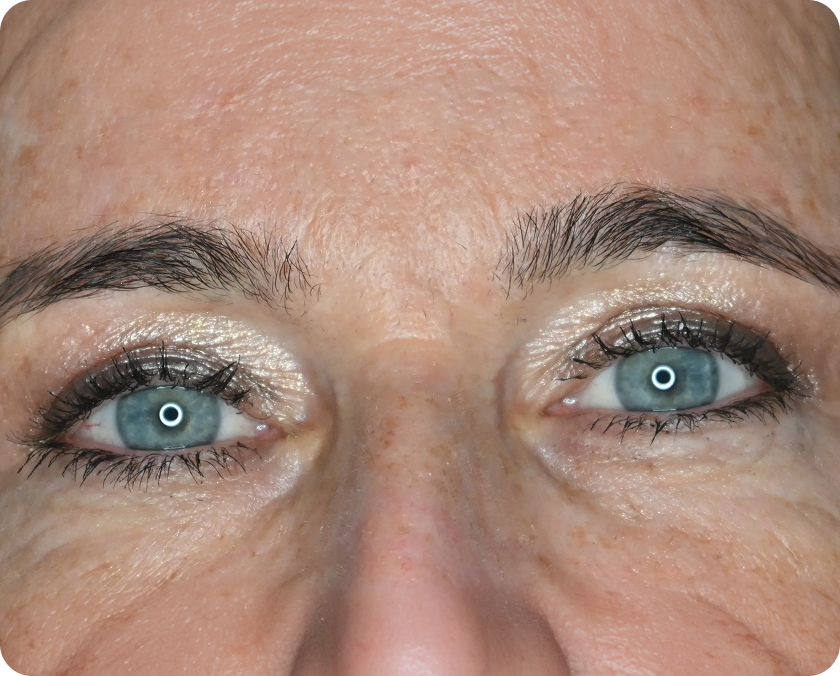 Nahaufnahme der blauen Augen einer Person mit schimmerndem Lidschatten, Wimperntusche und sichtbarer Hautstruktur und feinen Linien um die Augen.