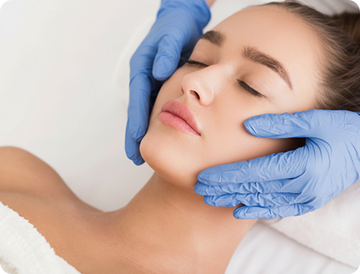 Eine Person mit geschlossenen Augen erhält eine Gesichtsbehandlung, während Hände mit blauen Handschuhen sanft ihr Gesicht berühren.