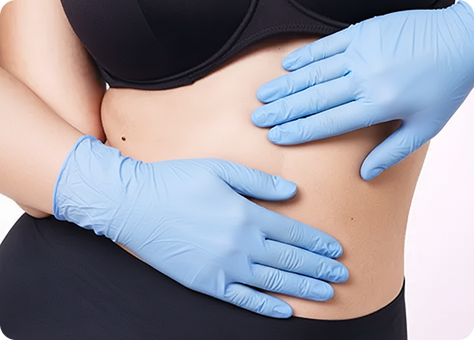 Eine Person mit blauen medizinischen Handschuhen berührt ihre nackte Körpermitte, die schwarz gekleidet ist, was auf einen medizinischen oder kosmetischen Eingriff hindeutet.
