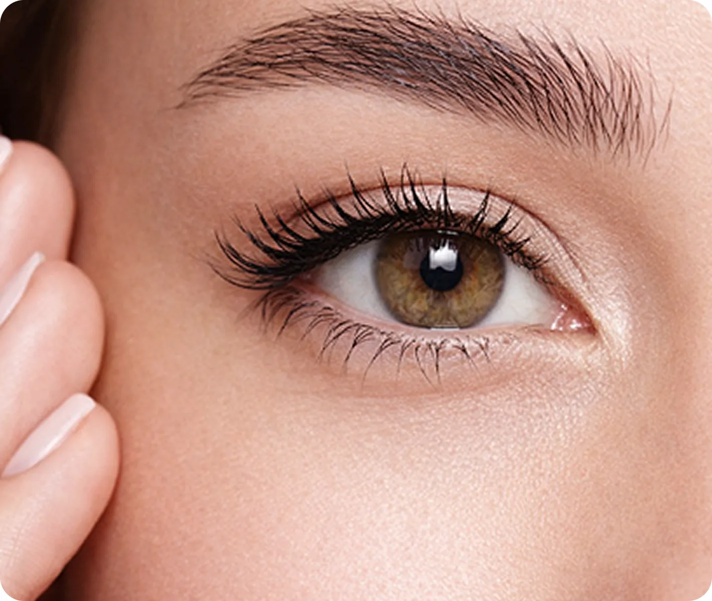 Nahaufnahme des grünlich-braunen Auges einer Person mit langen Wimpern und gepflegter Augenbraue, die Hand ruht neben dem Gesicht.