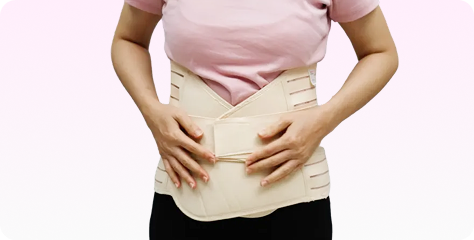 Person, die einen hellen Lendenstützgürtel über einem rosa Hemd und einer schwarzen Hose trägt und die Gurte mit beiden Händen verstellt.