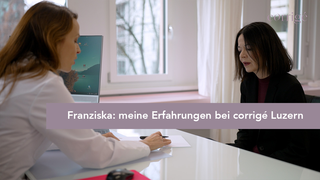 Eine Frau in einem weißen Kittel unterhält sich mit einer anderen Frau an einem Schreibtisch in einem hellen Büro. Der Text ist überlagert: "Franziska: meine Erfahrungen bei corrigé Luzern.